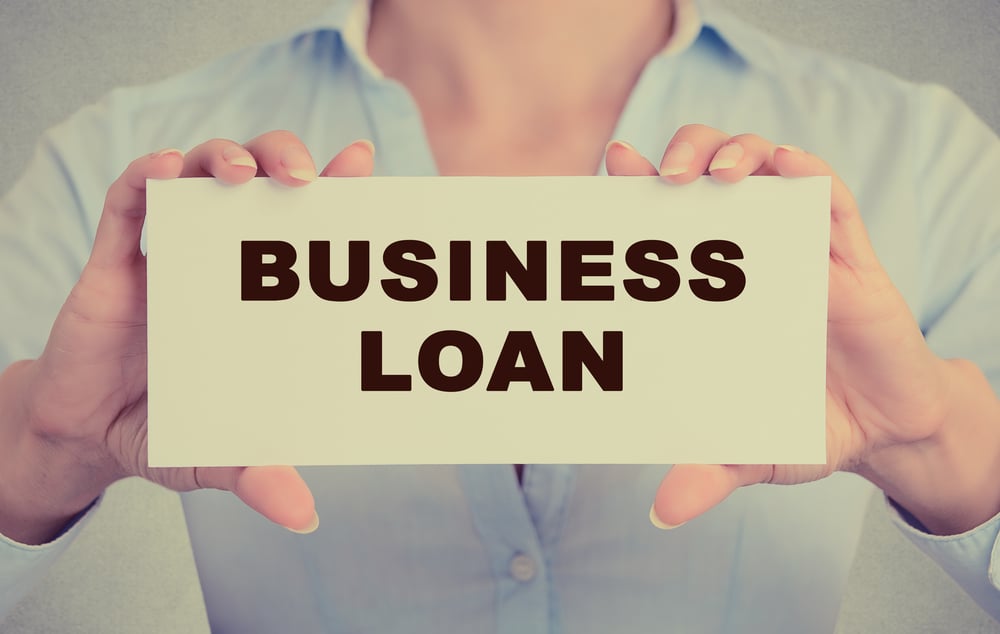 Business woman hands holding white card sign with business loan text message isolated on grey wall office background. Retro instagram style image Business woman hands holding white card sign with business loan text message isolated on grey wall office background. Retro instagram style image
